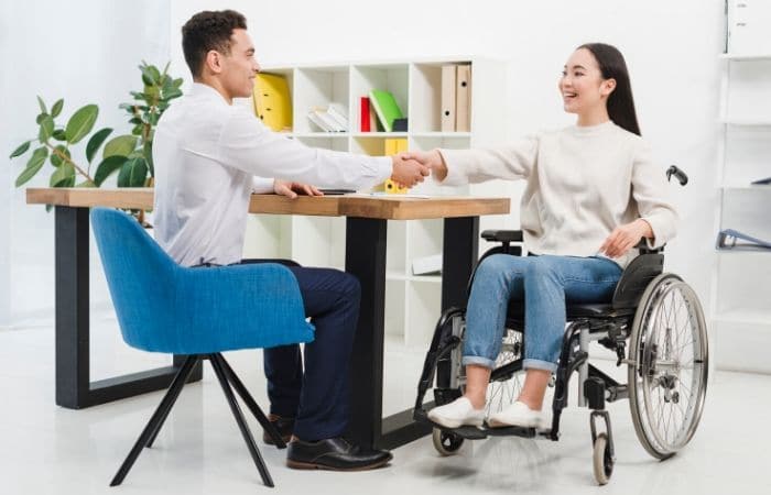 Man at his desk shaking the hand of a women in a wheelchair.