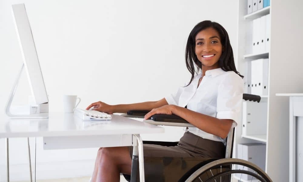 Women smiling using a computer in a wheelchair.